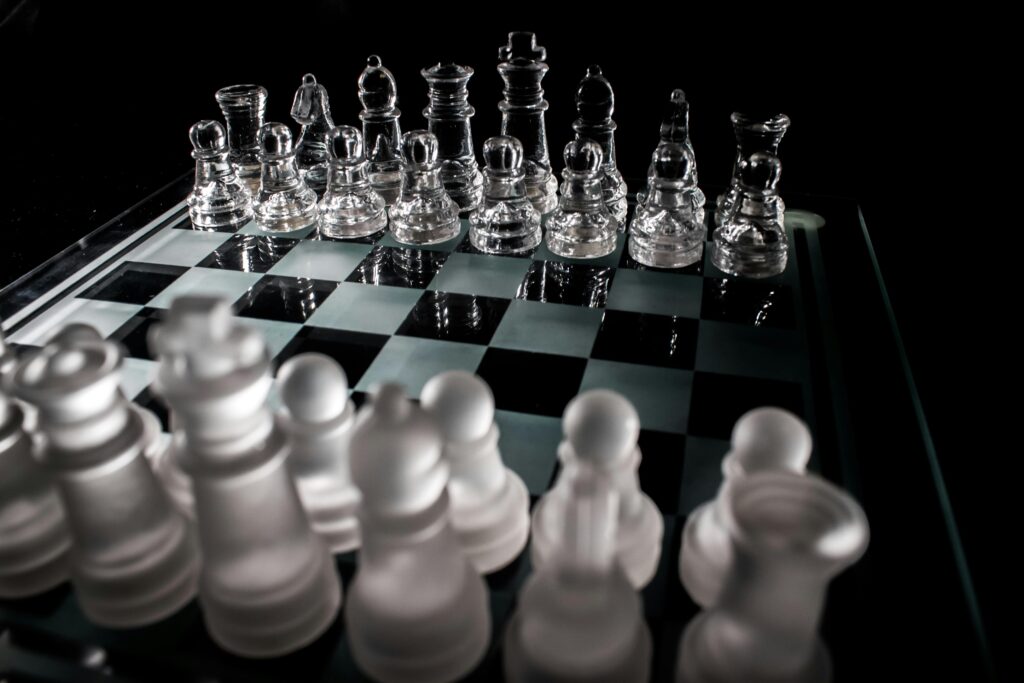 Glass chess pieces arranged on a reflective chessboard in a dark studio setting, symbolizing strategy and precision.