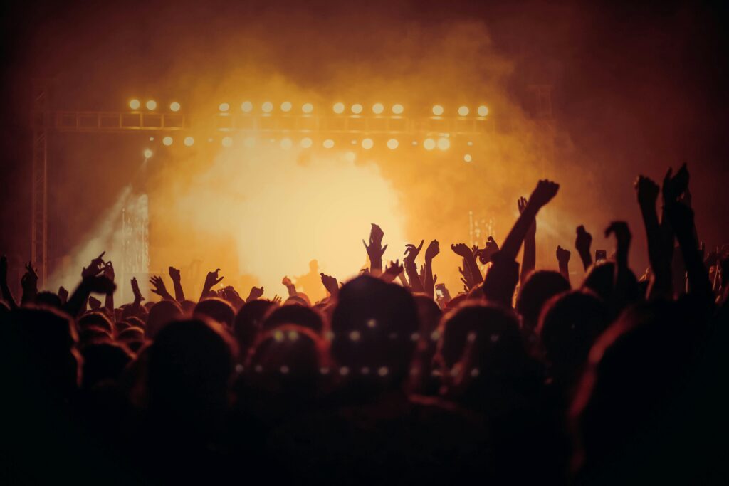 Silhouetted crowd at an exclusive nighttime concert event with warm golden stage lighting.